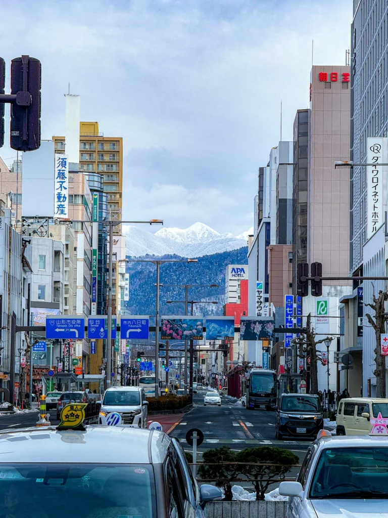 A city street in Yamagata lined with buildings looking toward snow-capped mountains