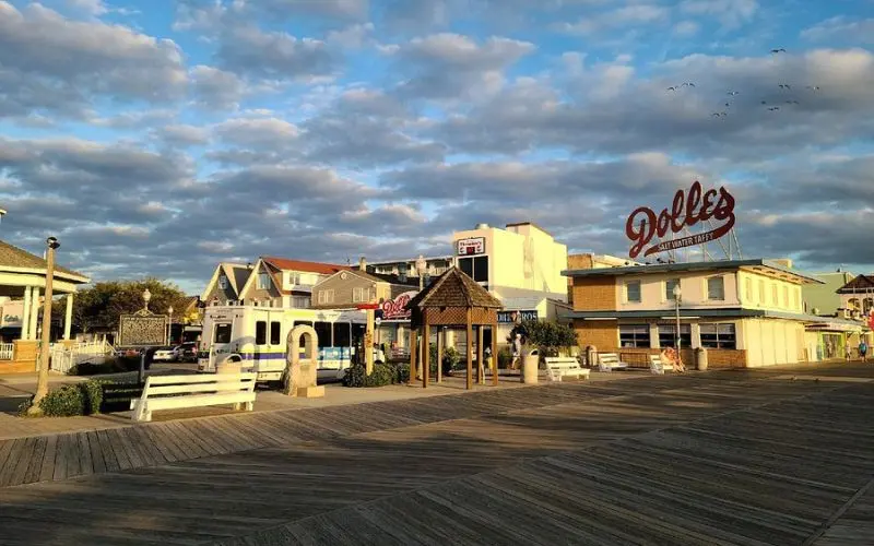 Rehoboth Beach Boardwalk with shops, benches, and the Dolles sign at sunset.