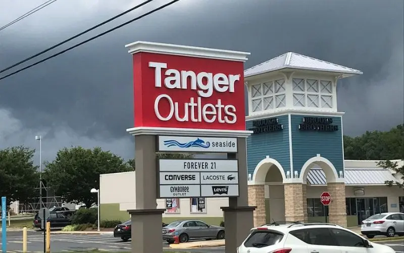 Tanger Outlets sign and shops under a cloudy sky.