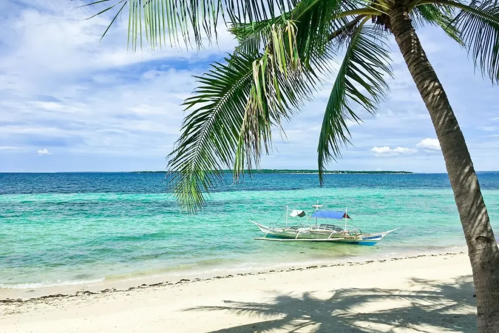 A white sand beach with a palm tree and boat on Bantayan Island.