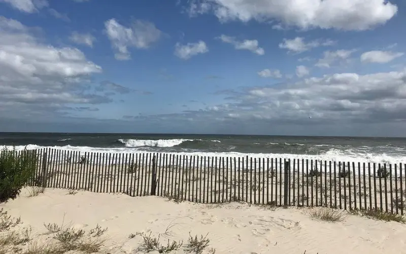 Sandy beach with wooden fencing and waves at Delaware Seashore State Park.
