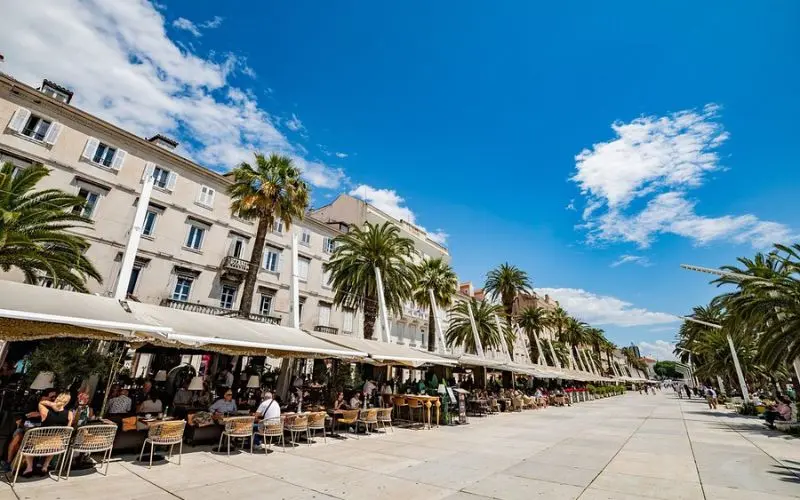 People enjoying cafes and walking along the palm-lined Riva Promenade in Split.