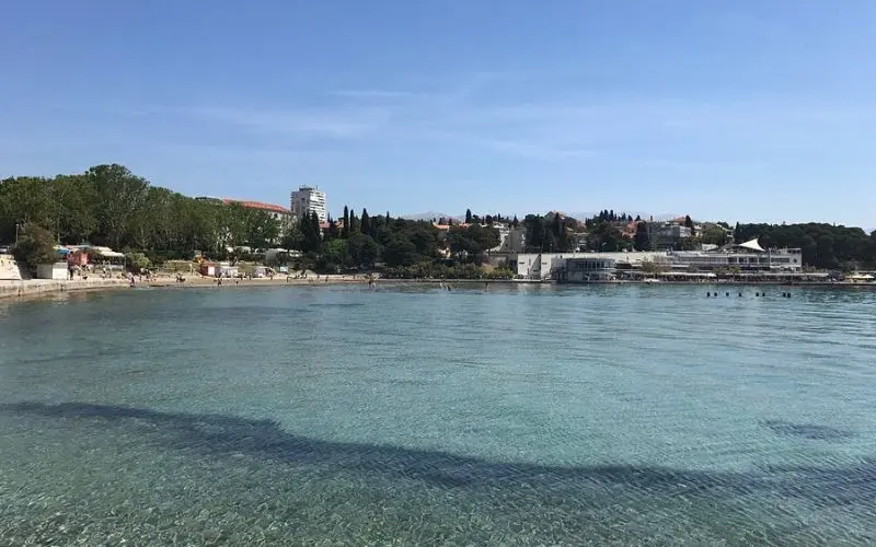 Clear shallow waters at Bačvice Beach with buildings in the background.