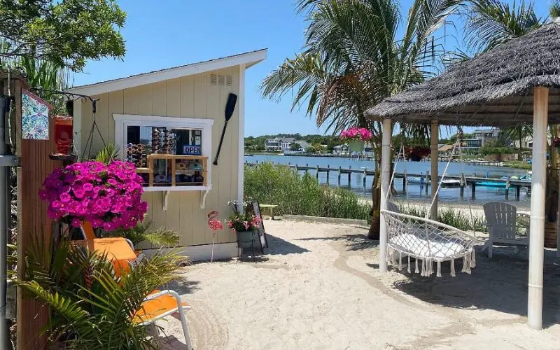 Relaxing sandy spot with flowers, a hut, and water views at Delmarva Board Sport Adventures.