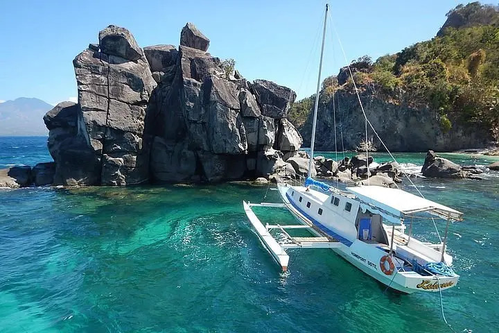 A white boat floating on clear turquoise waters near rocks at Mactan Island.