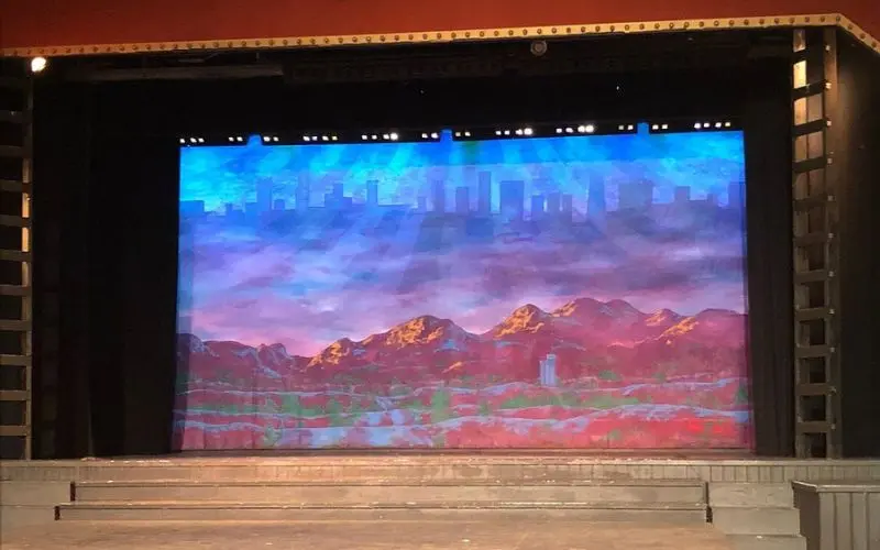 Clear Space Theatre stage with a painted backdrop of mountains and a city skyline.