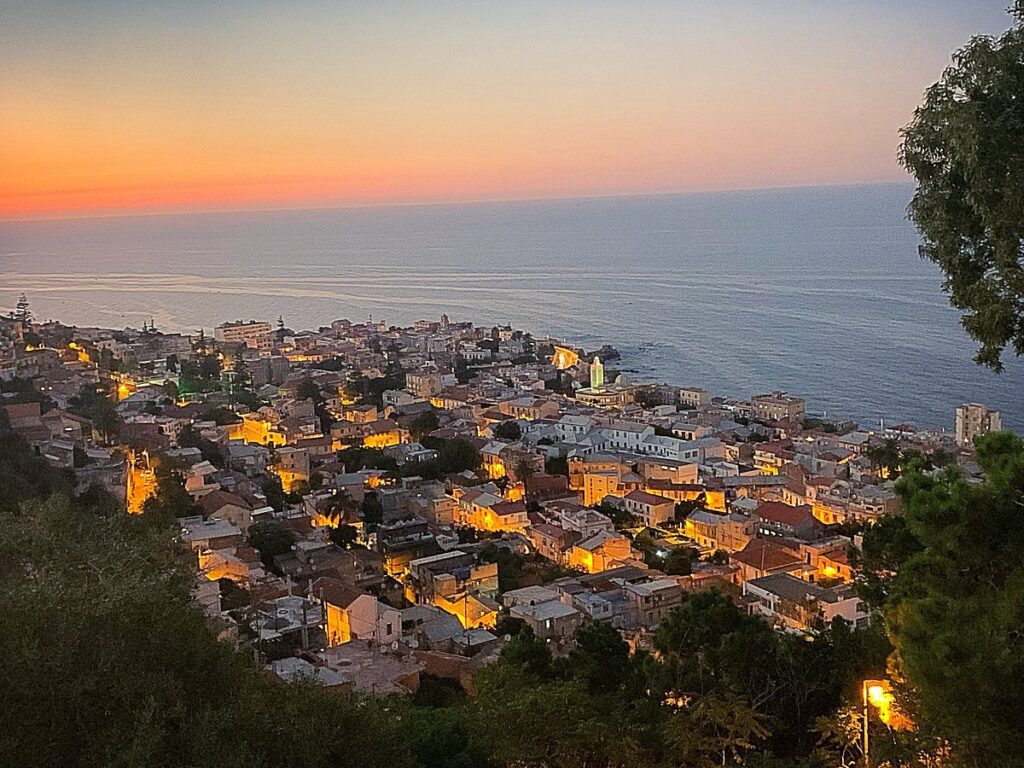 Sunset view over the city of Algiers with buildings lit up by evening lights.
