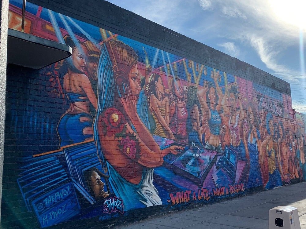 Colorful Arts District mural of a DJ with headphones playing music for a lively crowd.