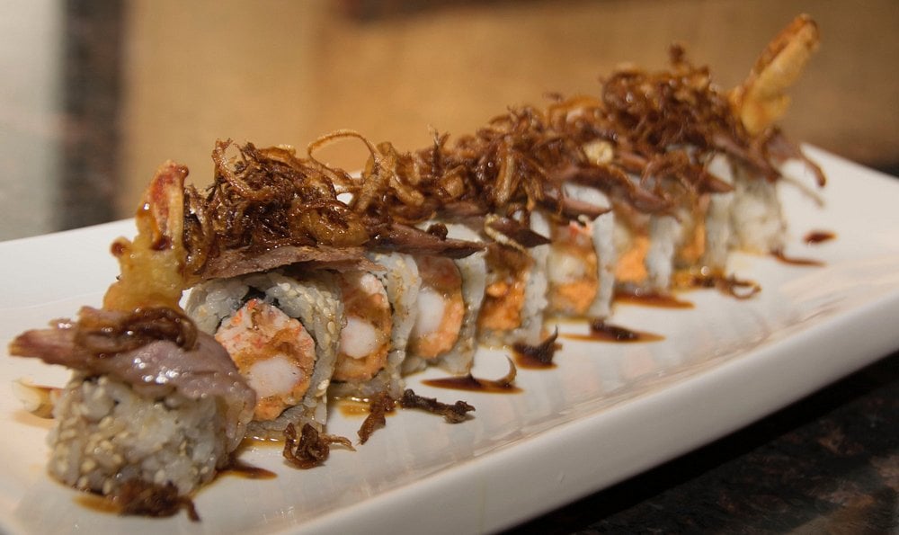 Sushi roll topped with crispy fried onions at Osae Sushi Ramen Bistro, served on a white plate.