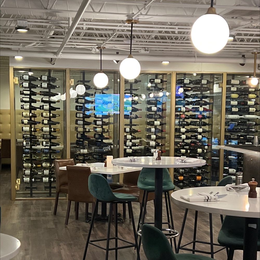 Sleek interior of TILL with modern lighting, velvet chairs, and a large glass wine display.