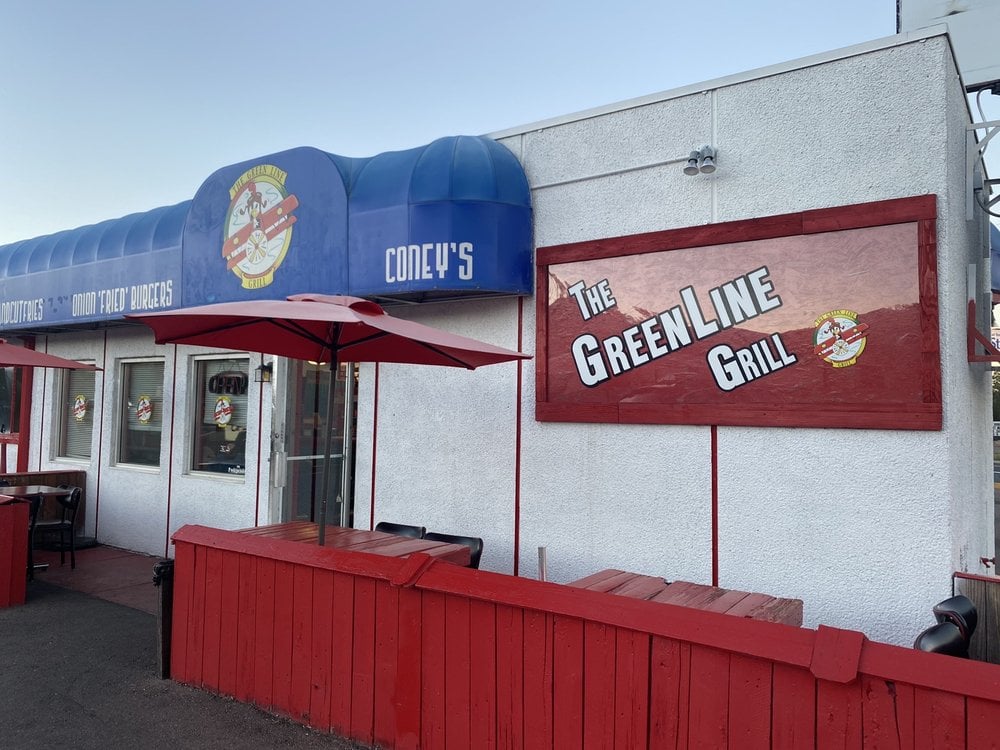 Exterior of The Green Line Grill with red patio seating and a bold sign on the wall.