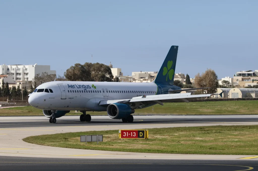 Aer Lingus Airbus A320 commercial passenger jet taxiing on an airport runway next to a yellow runway sign