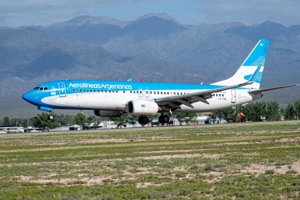 Aerolíneas Argentinas Boeing 737 airliner landing on a runway with mountains in the background