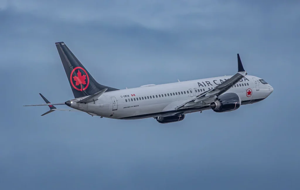 An Air Canada Boeing 737 MAX 8 commercial airplane flying against a dark blue sky