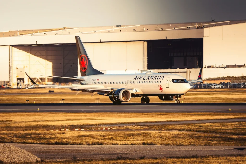 Air Canada Boeing 737 MAX 8 aircraft taxiing on the runway in front of an airport hangar during golden hour