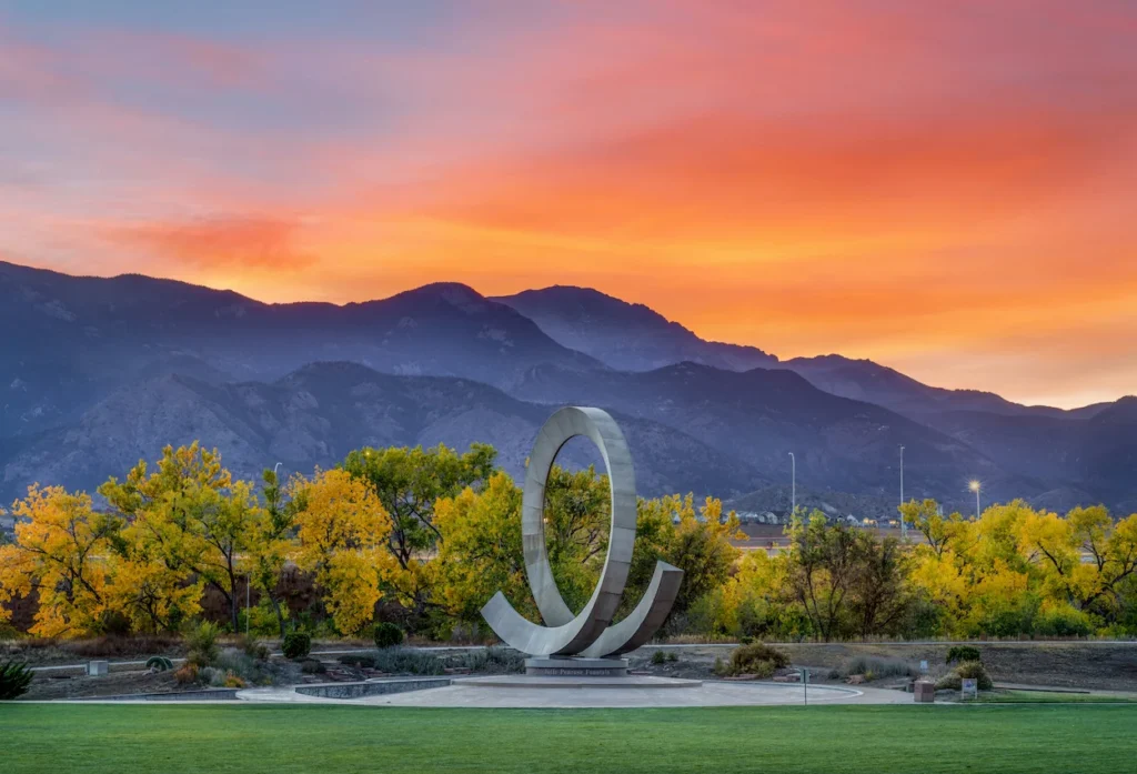 Julie Penrose Fountain ring sculpture with yellow autumn trees and mountains during an orange sunset