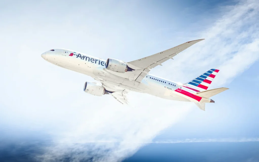 An American Airlines Boeing 787-8 Dreamliner passenger plane banking sharply as it climbs through white clouds into a blue sky