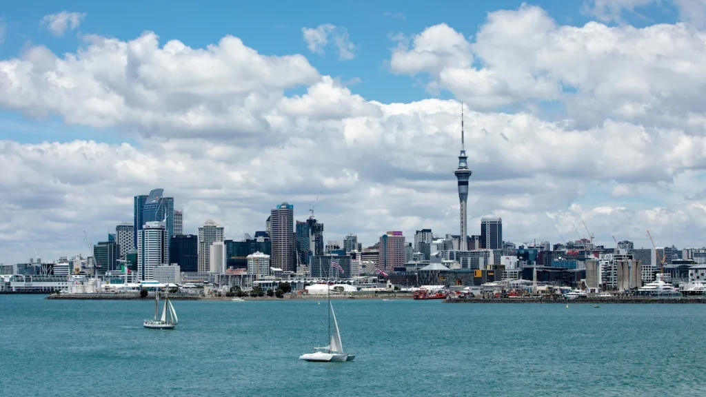 Auckland city skyline and Sky Tower tower across blue harbor water with two small white sailboats