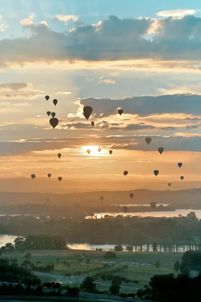 Hot air balloons floating over Lake Burley Griffin and the city landscape during a hazy golden sunrise