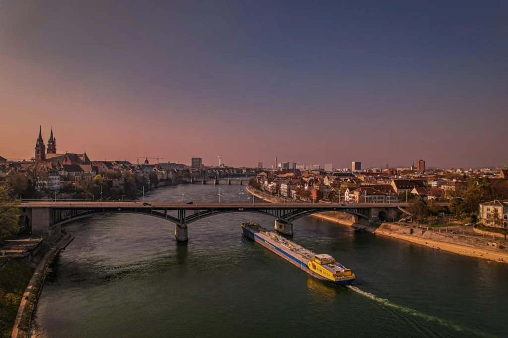 A cargo barge navigating the Rhine River near the Basel Minster in Switzerland
