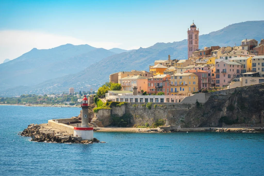 Stone jetty and red-topped lighthouse near cliffside coastal buildings in Bastia, France