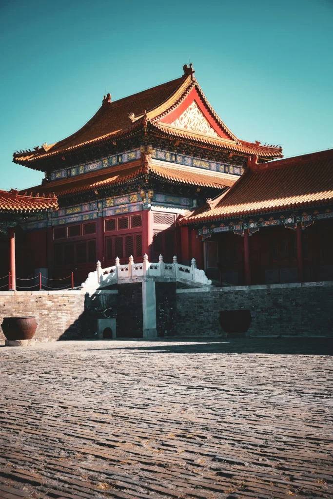Forbidden City courtyard with carved stone bridge, traditional red palace buildings, and large iron water vats
