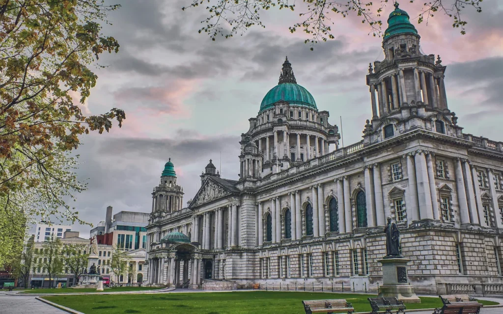 Belfast City Hall showing its green copper dome and towers under a sunset sky
