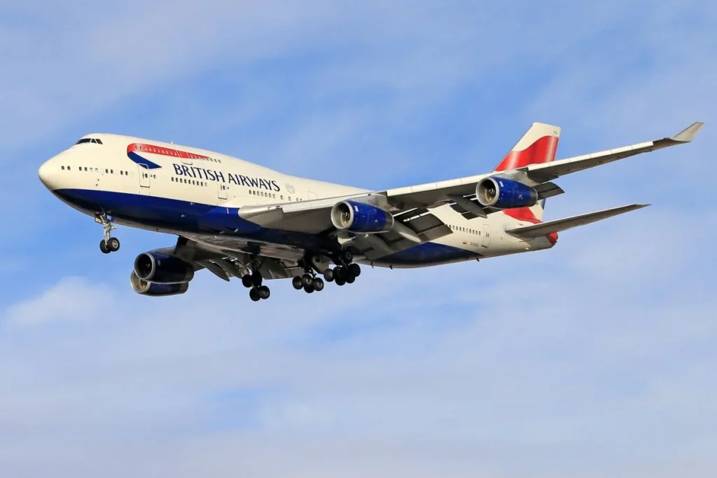 A British Airways Boeing 747-400 double-decker passenger airplane descending through a blue sky on final landing approach