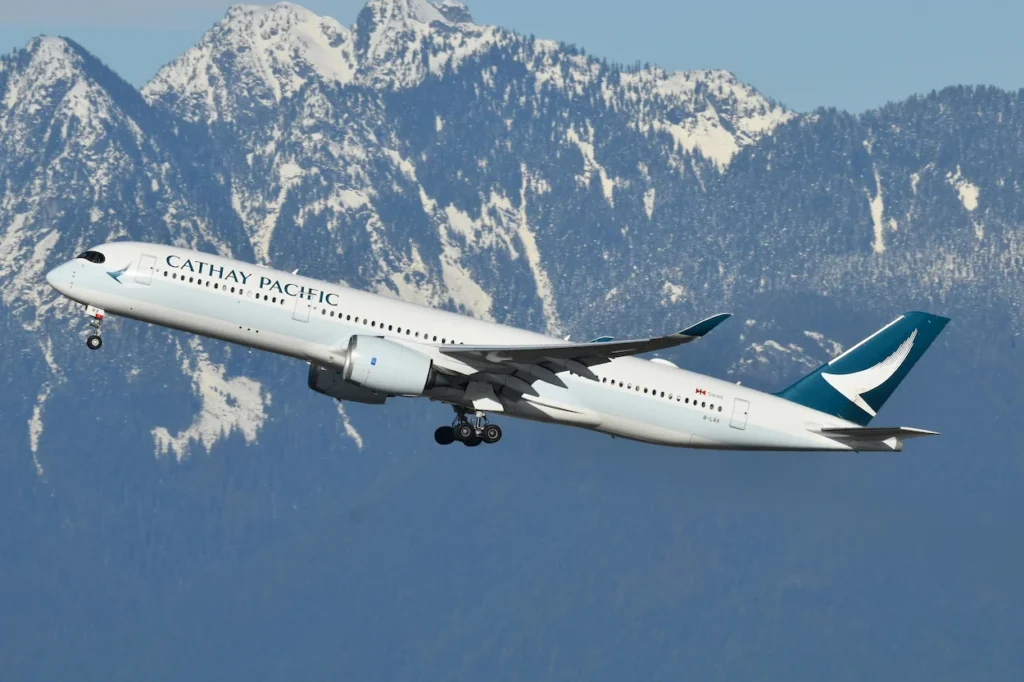 Cathay Pacific Airbus A350 passenger airplane climbing into the sky against snow-covered mountains