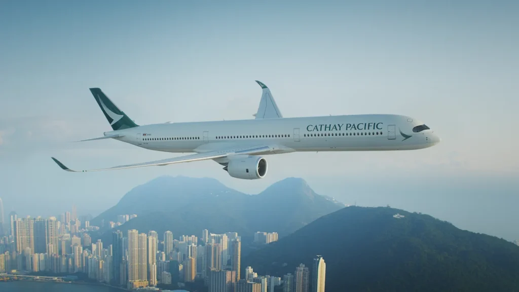 A Cathay Pacific Airbus A350 flying above Hong Kong's skyline and surrounding mountains