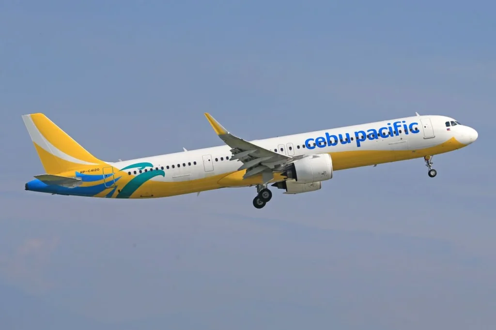 A yellow and white Cebu Pacific airplane flying in a blue sky