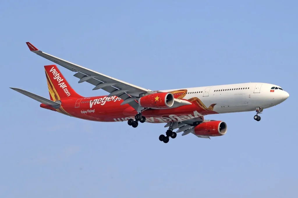 A red and white VietJet Air Airbus A330 widebody airplane preparing to land against a clear blue sky