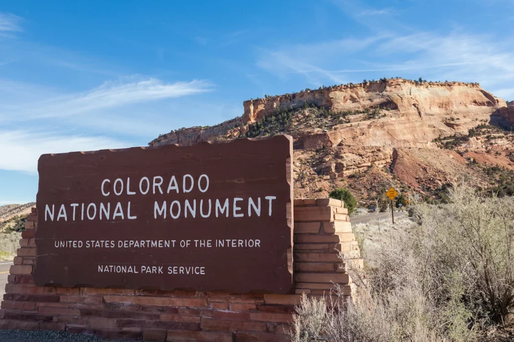 Wooden Colorado National Monument entrance sign with a red rock plateau behind it