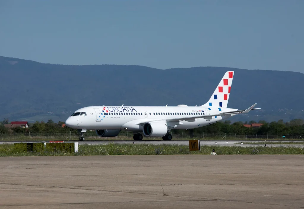 A Croatia Airlines Airbus A220-300 taxiing on an airport runway under a clear sky
