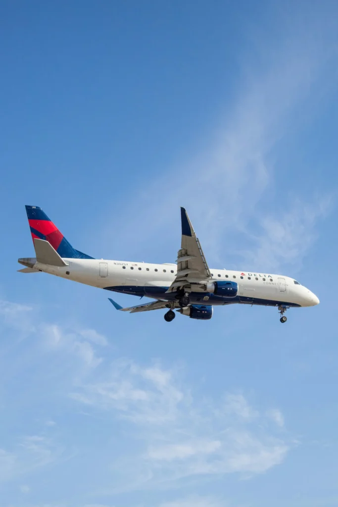 A Delta Connection Embraer E175 regional jet with landing gear extended flying across a bright blue sky