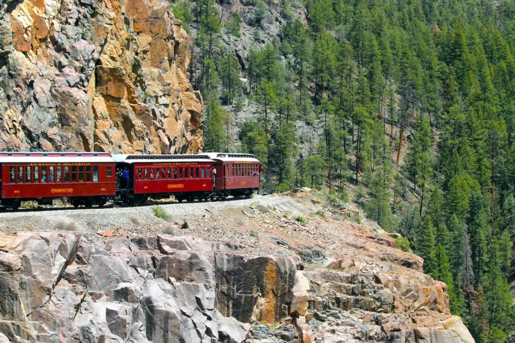 Red passenger cars of Durango and Silverton Narrow Gauge Railroad traversing a rocky cliffside track above a pine forest