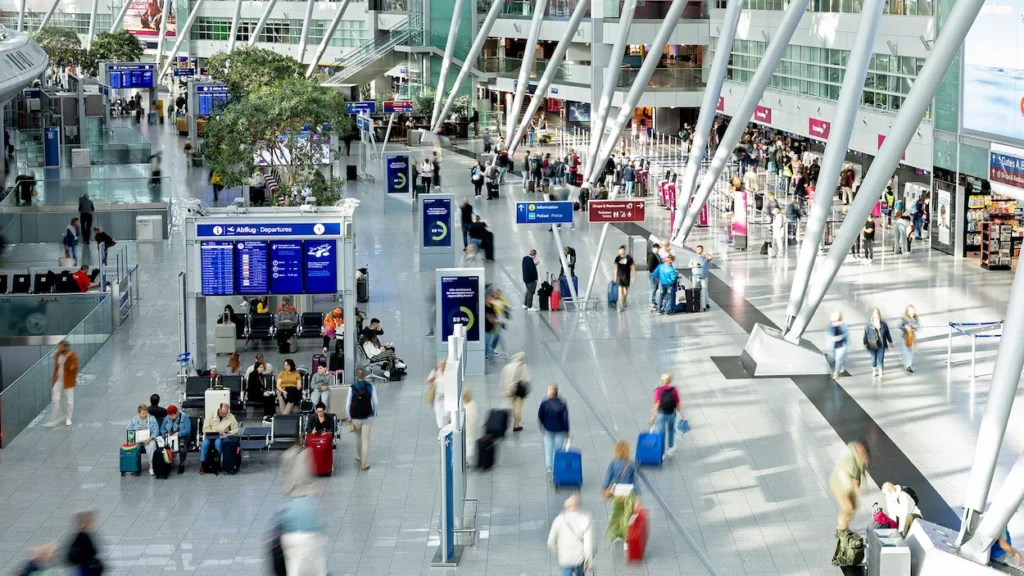 Busy main terminal at Düsseldorf Airport with passengers walking past departure screens and check-in areas