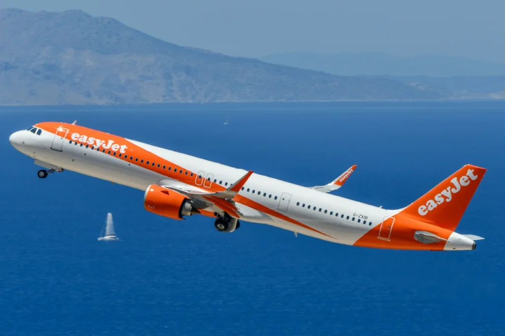EasyJet Airbus A321neo airplane climbing steeply over blue water during takeoff