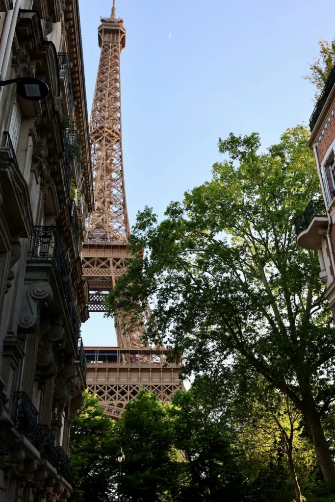 Low-angle view of the Eiffel Tower rising between classical Parisian buildings and green leafy trees
