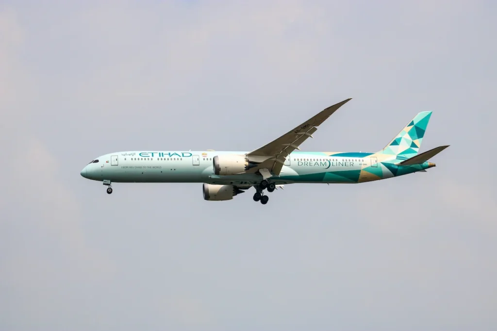 Etihad Airways Boeing 787 Dreamliner in its green and blue geometric Greenliner livery flying in a cloudy sky