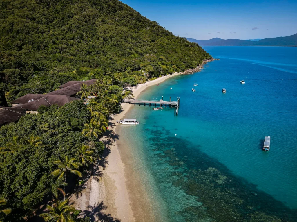 Fitzroy Island Resort aerial view showing the sandy beach, wooden jetty, and turquoise waters