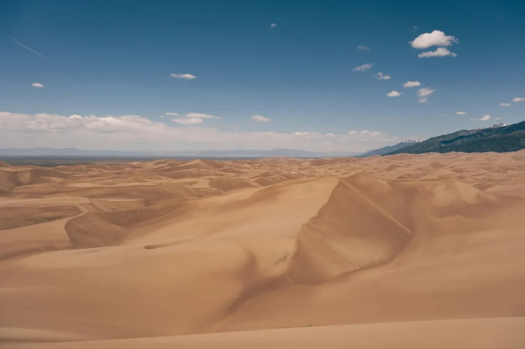 Vast rolling sand dunes extending toward mountains under a blue sky at Great Sand Dunes National Park