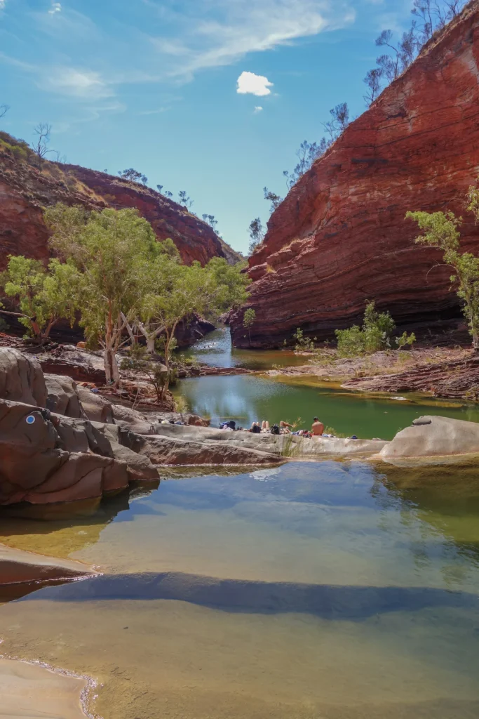 Natural green swimming hole enclosed by layered red rock cliffs in Hamersley Gorge