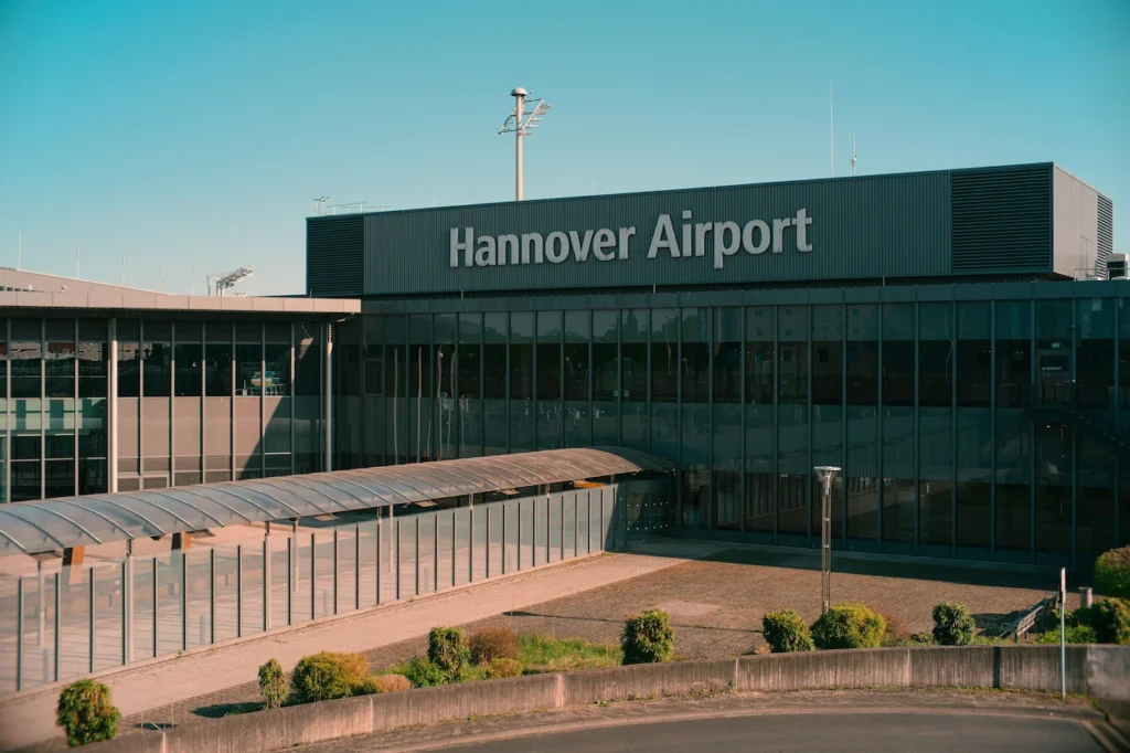 Exterior terminal building facade featuring the large sign Hannover Airport under a clear blue sky