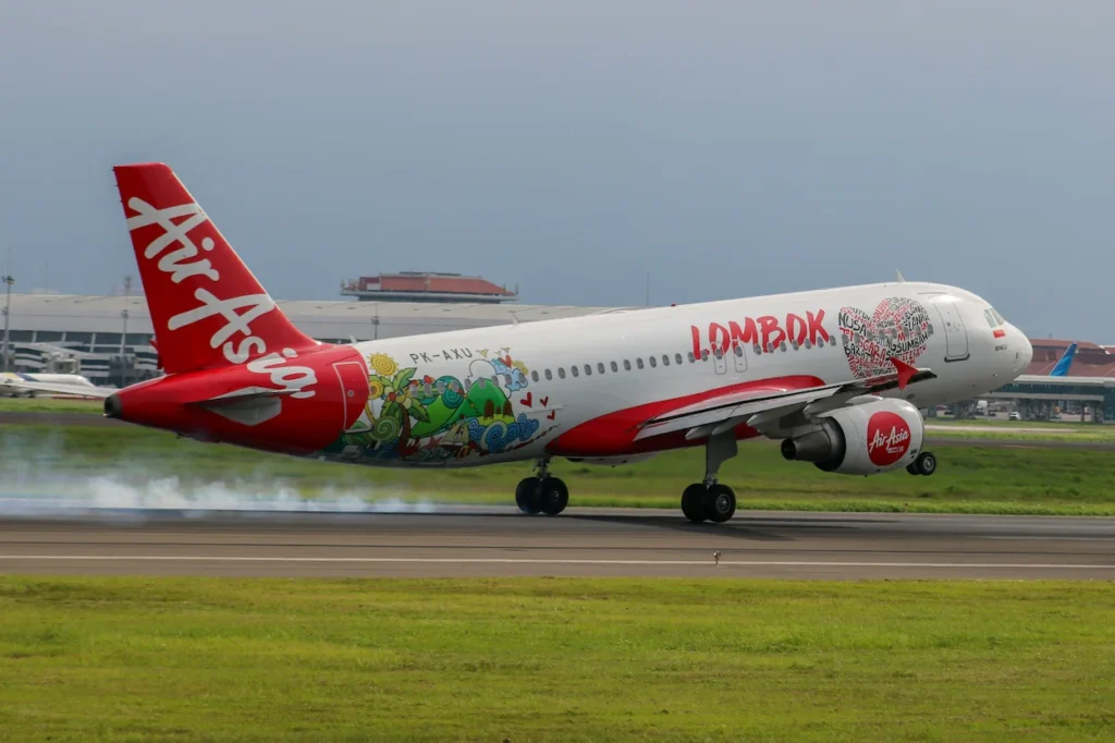 Indonesia AirAsia Airbus A320 plane with a special red and white Lombok livery landing on a runway