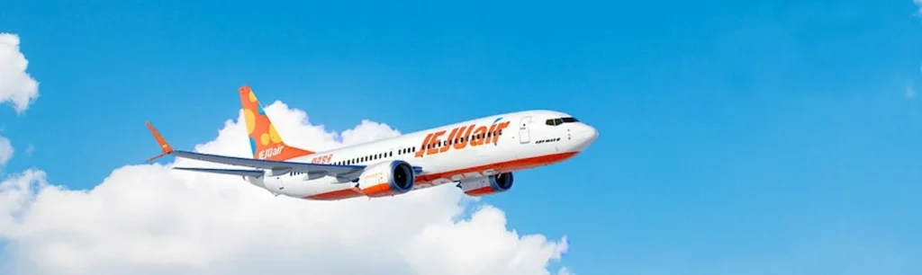 Jeju Air Boeing 737 passenger airplane flying in a bright blue sky above white clouds
