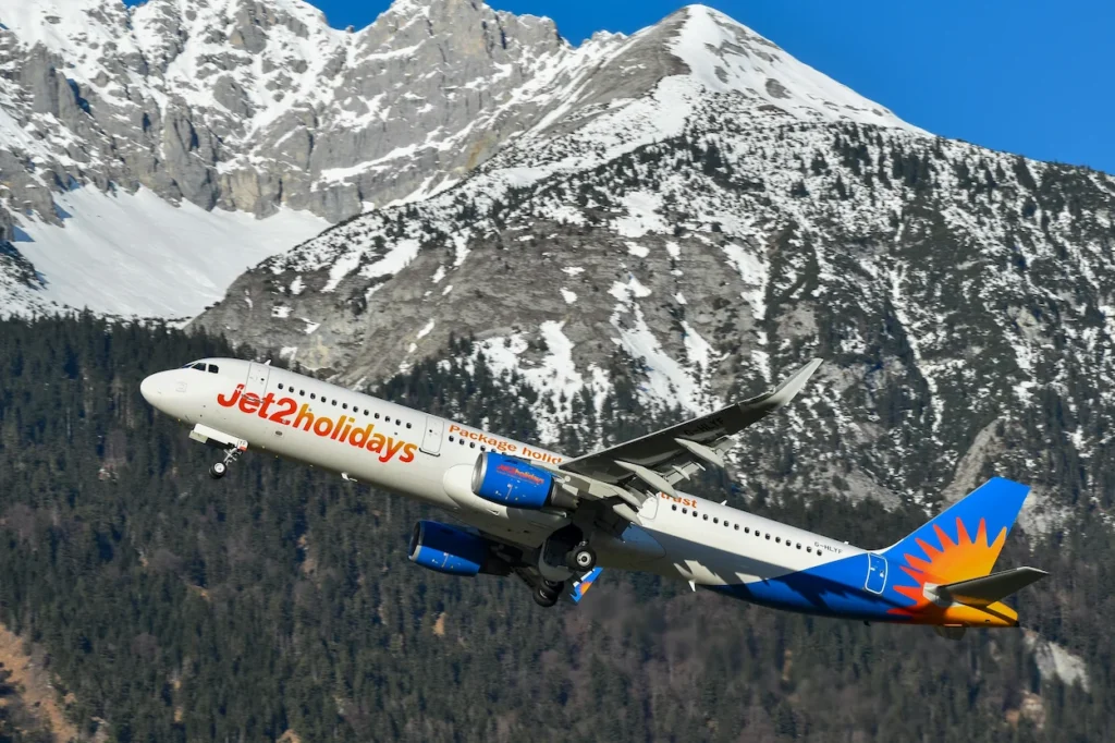 Jet2holidays Airbus passenger airplane taking off with landing gear extended in front of snow-capped alpine mountains