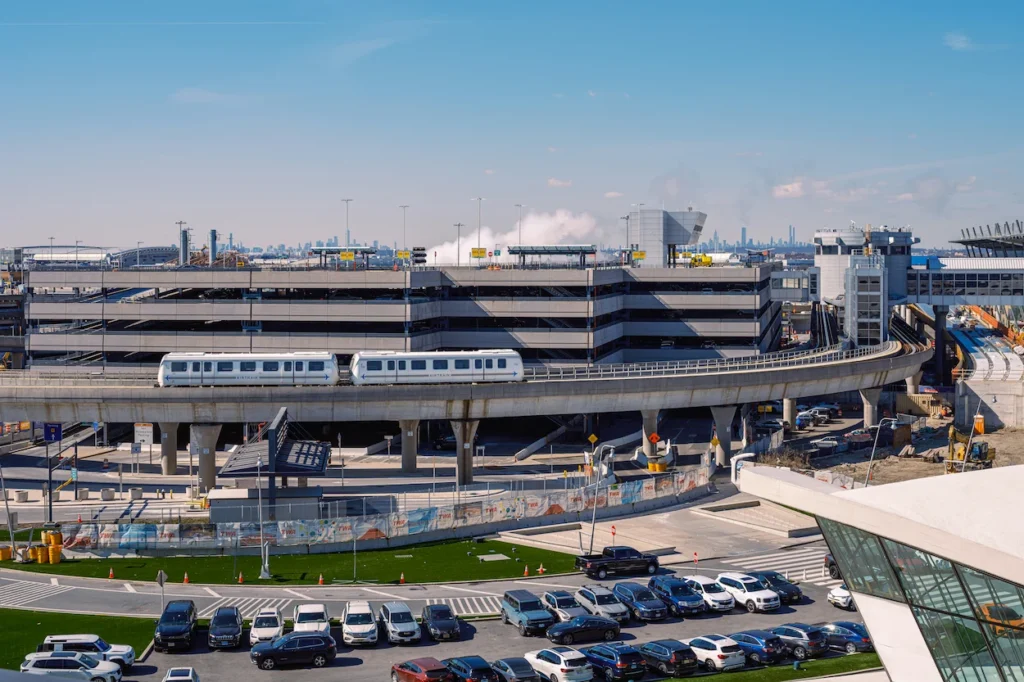 JFK AirTrain traveling on an elevated track past a parking garage