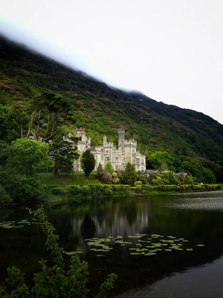 Kylemore Abbey castle building reflecting on calm lake water with a misty mountain backdrop
