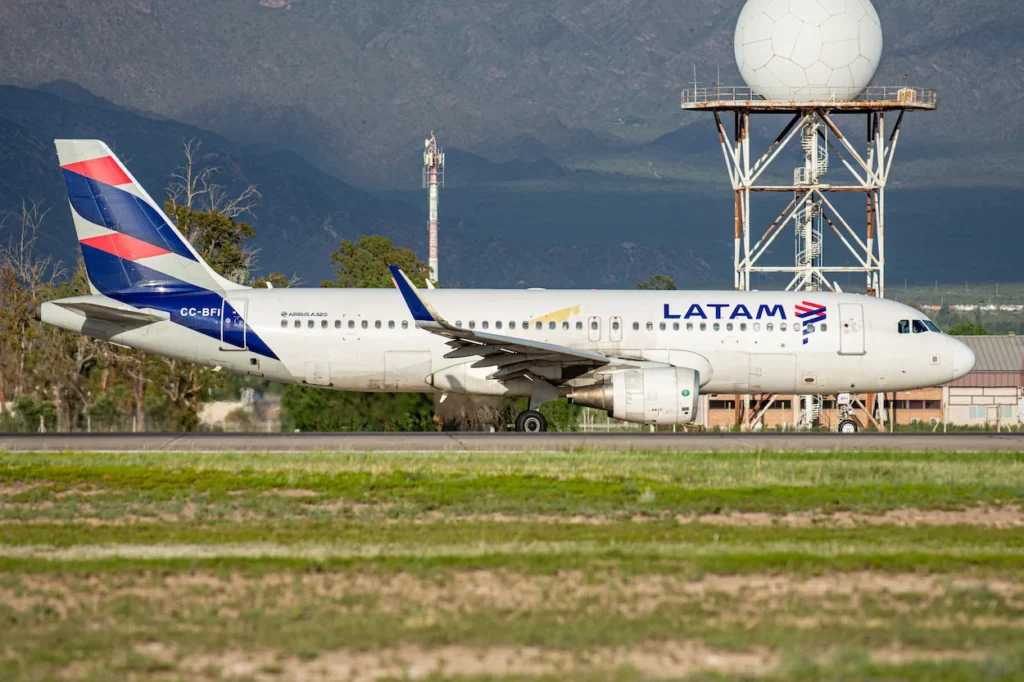 A LATAM Airlines Airbus A320 commercial airplane taxiing on a runway with a large white radar dome and mountains in the background